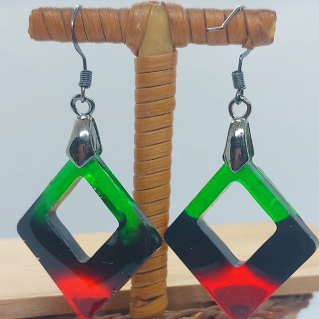 Pair of earrings with green and red square design on a wooden stand.
