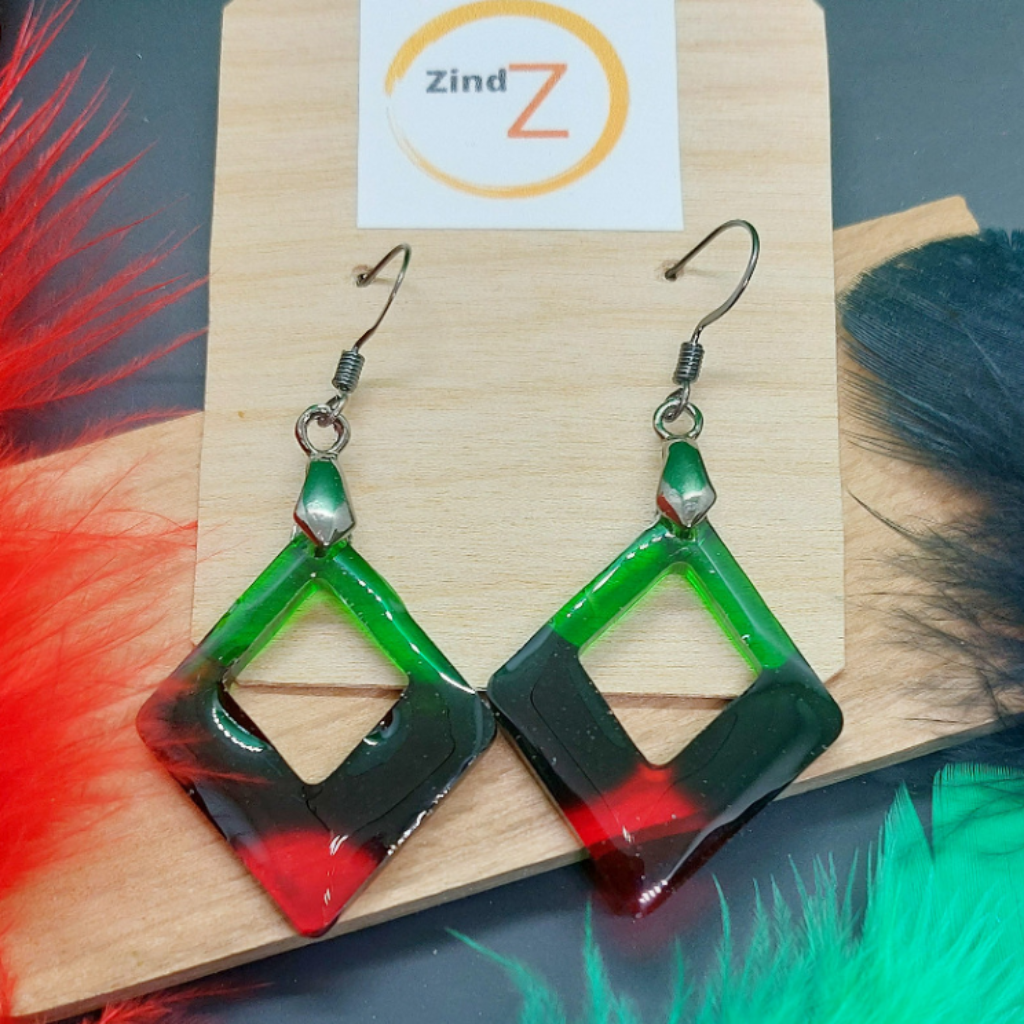 Green and red geometric earrings on a wooden stand with Zind brand card.