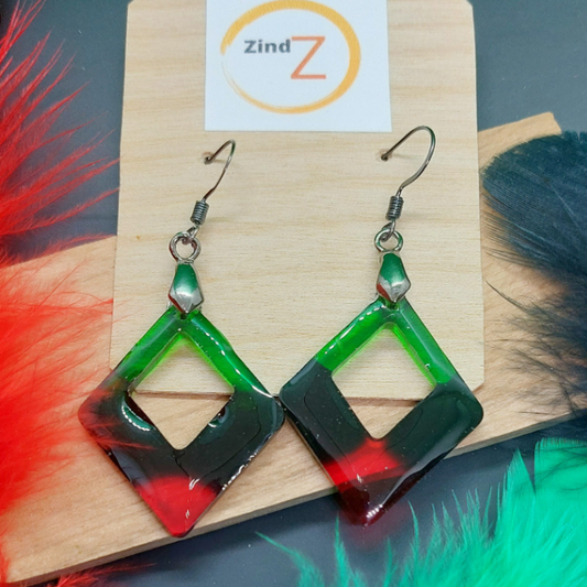 Green and red geometric earrings on a wooden stand with Zind brand card.