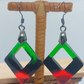 Pair of earrings with green and red square design on a wooden stand.